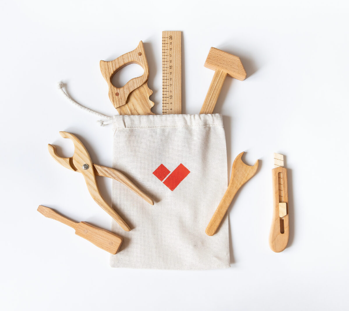 Set of wooden tools including a hammer, wrench, pliers, and a ruler on a white background with a branded drawstring bag.