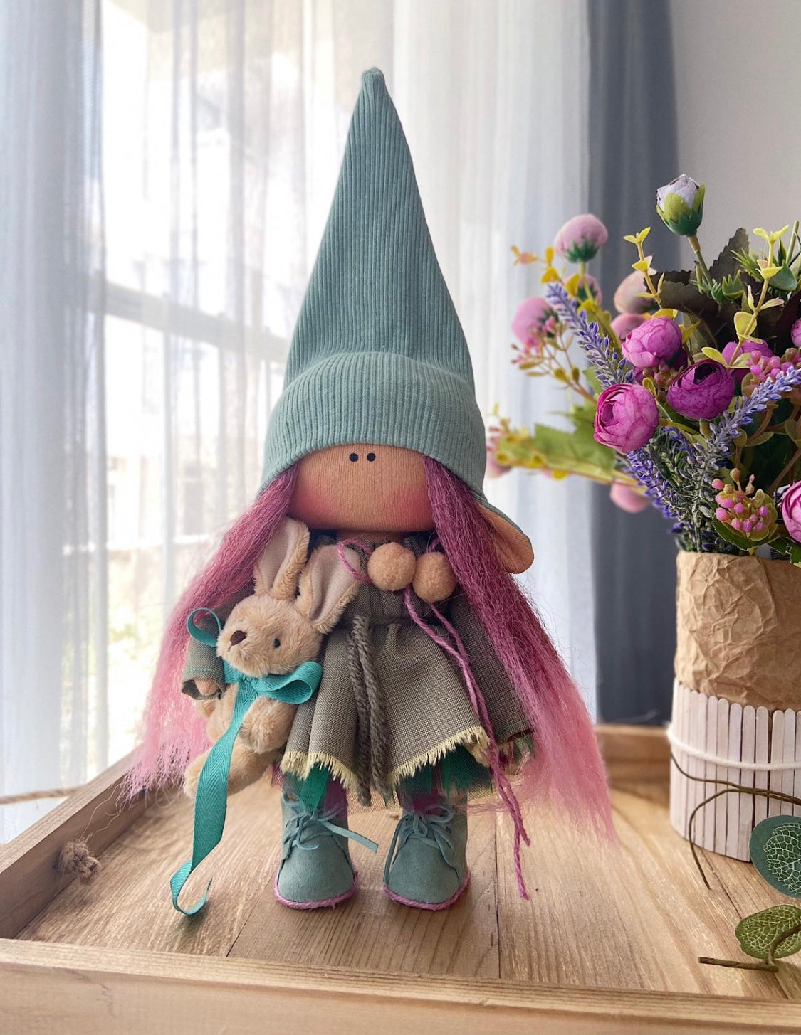Gnome figurine with pink hair and a green hat on a wooden surface with flowers in the background