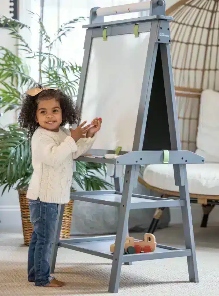A little girl standing in front of an art easel and smiling at the camera.