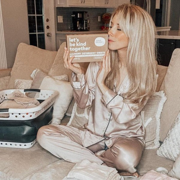 A blond woman in her pajamas holding a box of Kind Laundry Detergent Sheets