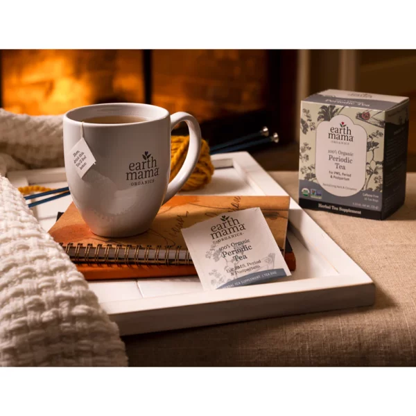 A mug of warm tea sitting on a stack of notebooks and journals in front of a fireplace.