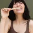 A woman in a bathroom smiling brushing her teeth with charcoal and mint toothpaste tablets.