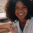 A young woman smiling and holding a Badger Cocoa Butter Lip Balm in Cool Mint flavor