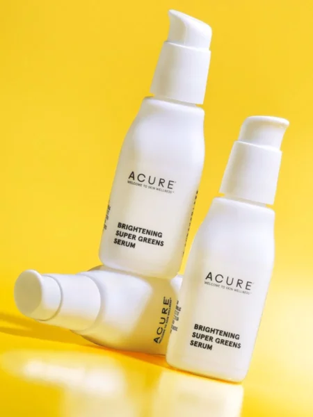 An image of 3 bottles of Acure Brightening Super Greens Serum on a yellow background