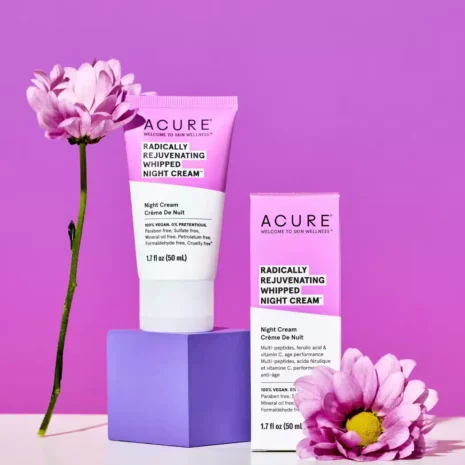 An image of Acure Radically Rejuvenating Whipped Night Cream sitting on a pink background with pink daisy flowers