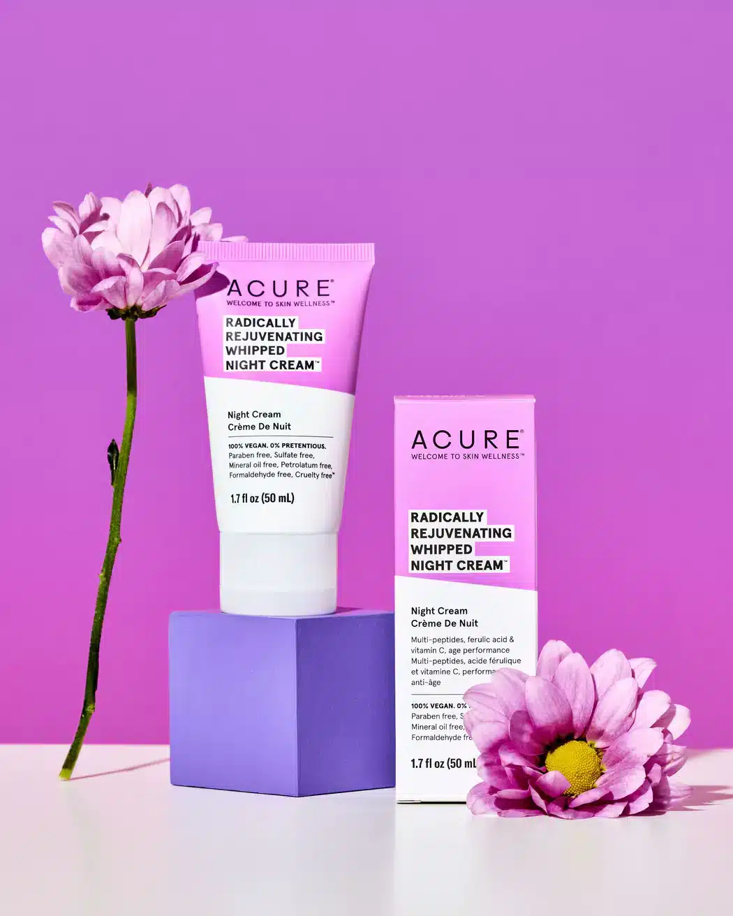 An image of Acure Radically Rejuvenating Whipped Night Cream sitting on a pink background with pink daisy flowers