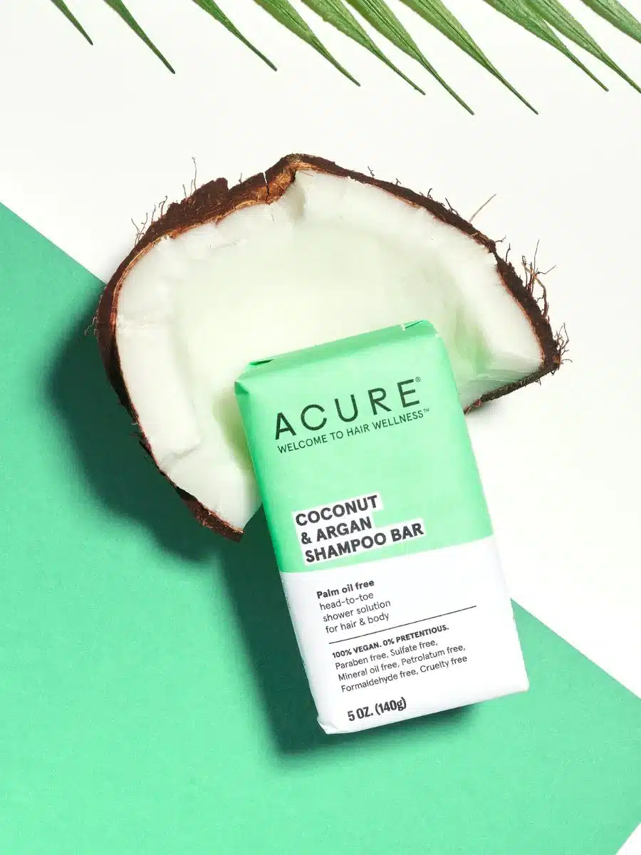 An image of Acure Natural Shampoo Bar sitting in a piece of coconut on a green and white background