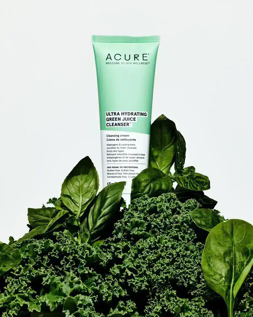A bottle of Acure Ultra Hydrating Green Juice Cleanser on a pile of kale and spinach.