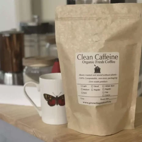 A bag of organic fresh coffee sitting in front of a mug and a coffee pot.