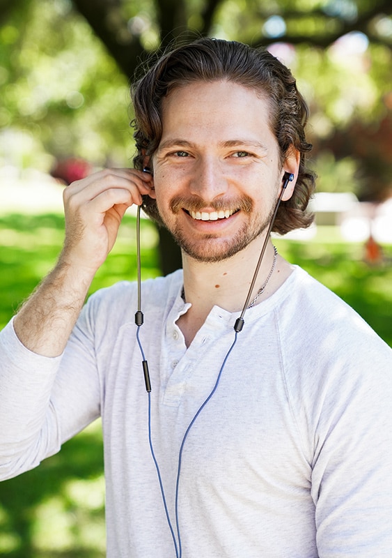 A man smiling and standing outside while listening to DefenderShield Air Tube EMF Radiation Blocking Headphones.