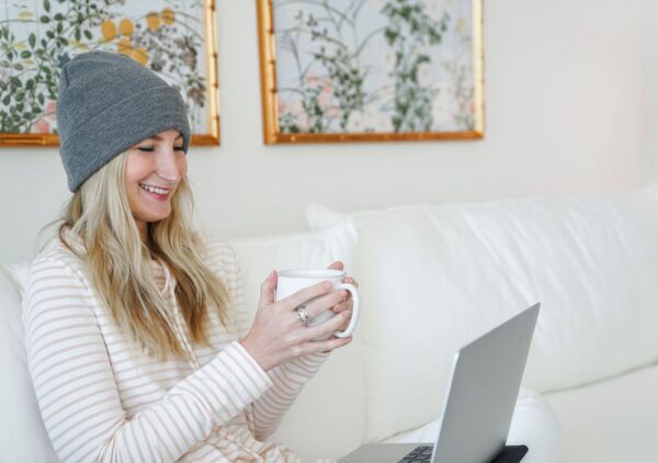 A woman sitting on a couch holding a mug and wearing a emf protection hat and smiling.