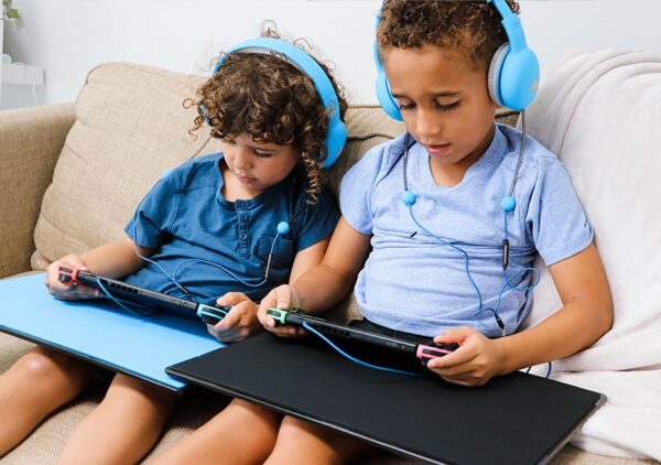 Two young boys with curly hair sitting on the couch and listening to blue over-ear headphones.