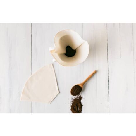An image of a reusable cotton coffee filter with fresh coffee grounds and beans on the table and in the filter.