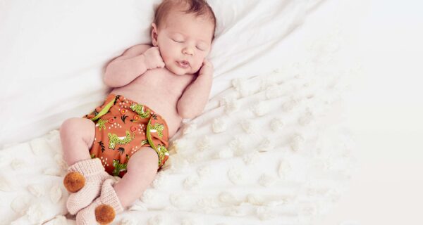 A baby sleeping on a white pillow and wearing an orange cloth diaper.