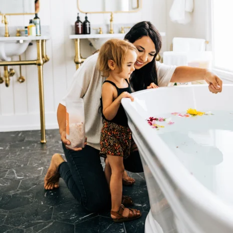 A woman and her daughter standing at the edge of a full bath tub and smiling.