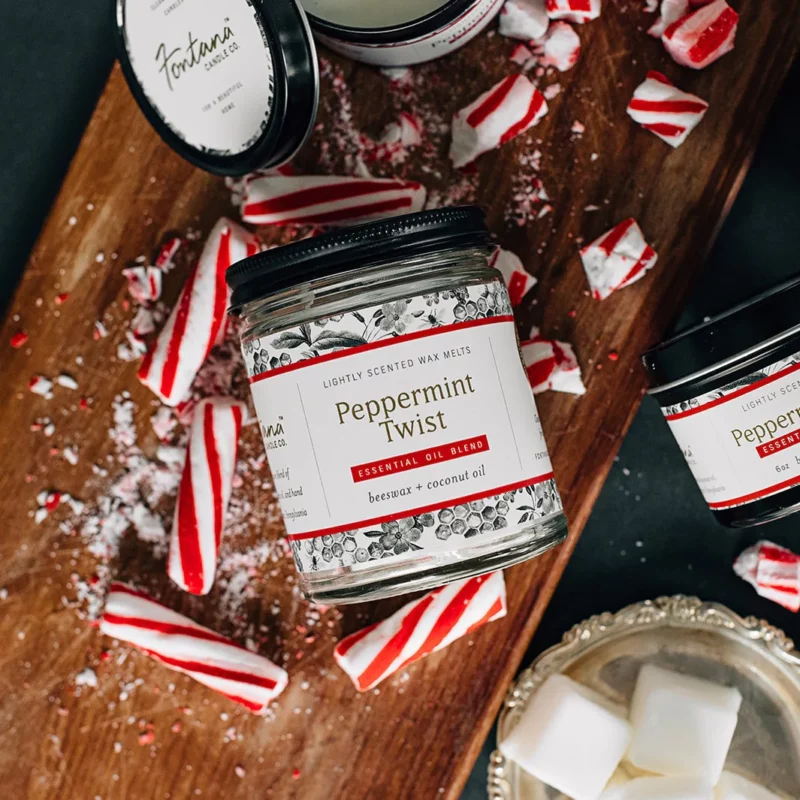 A glass jar candle sitting on a table with many pieces of broken peppermint sticks.