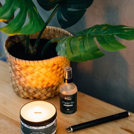 A bottle of Fontana Essential Oil Room Spray sitting on a table next to a potted house plant and a wax candle.