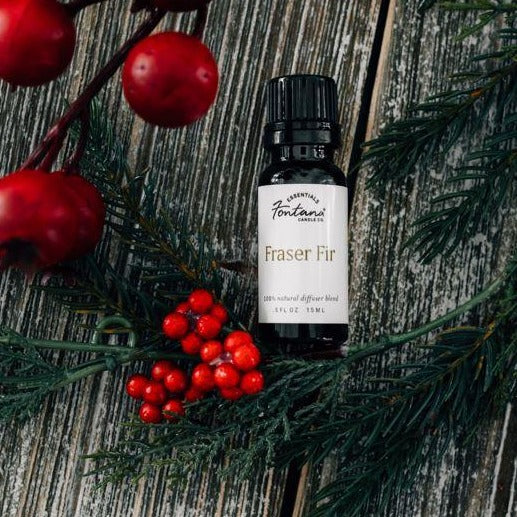 A small bottle of essential oil sitting next to holly shrubs.