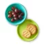 A blue silicone bowl filled with purple grapes and a green silicone plate with crackers.