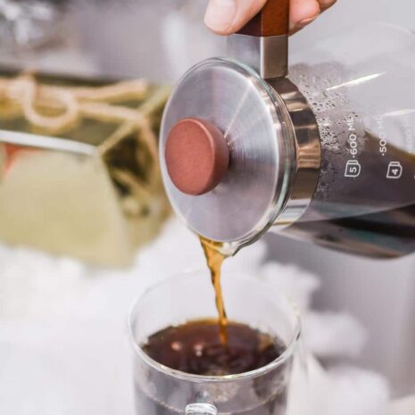 A pour over coffee pot pouring fresh coffee into a glass mug.