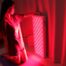 A woman kneeling in front of a red light therapy panel.