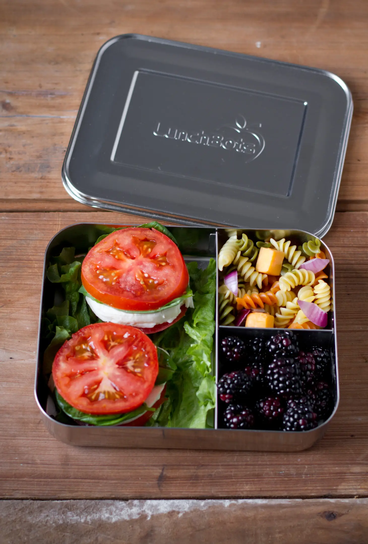 https://gimmethegoodstuff.org/wp-content/uploads/LunchBots-Large-3-Compartment-Stainless-Steel-Bento-Lunchbox-on-a-wooden-table-filled-with-blackberries-pasta-salad-and-tomatoe-sandiwches..webp