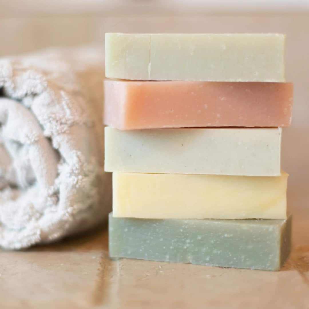 A stack of 5 different Moon Valley Organics Shampoo bars sitting on a tile ledge with a towel