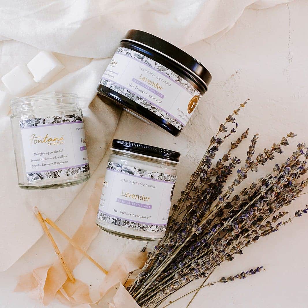 Several sizes of non-toxic essential oil candles sitting on a white surface with lavender.