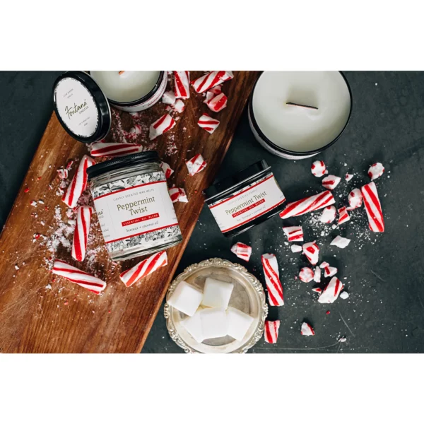A collection of differently sized candle tins sitting on a cutting board surrounded by peppermint sticks.