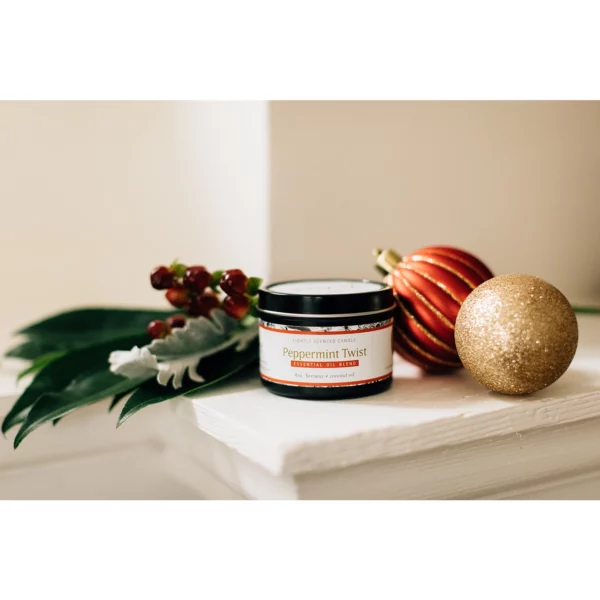 A non toxic candle sitting on a sill with holiday decorations including two small pumpkins