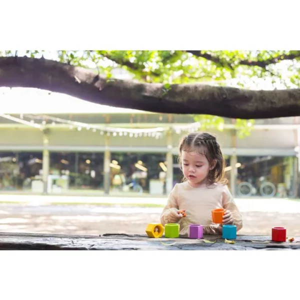 A young girl sitting outside and playing with a Plan Toys Beehives Wooden Block Game