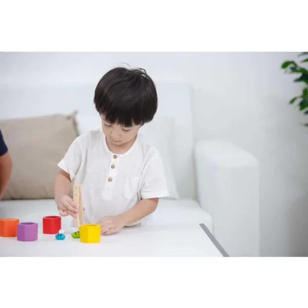 A young boy sitting in a white living room and playing with Plan Toys beehives wooden block game.