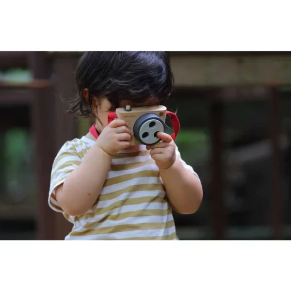 A young boy holding a wooden camera toy up to his eye and pretending to take a picture.