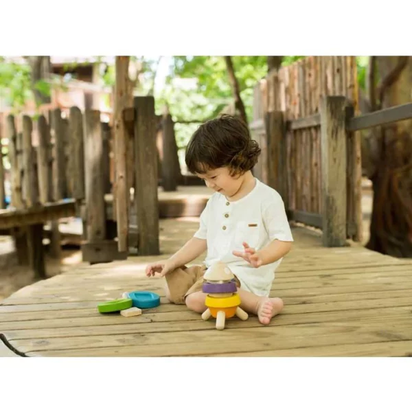 A young girl sitting on a deck and playing with a colorful wooden stacking toy shaped like a rocket.