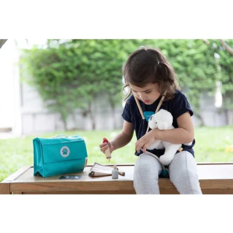 A young girl sitting outside on a bench playing with a stuffed dog toy and a pretend veterinary toy set.