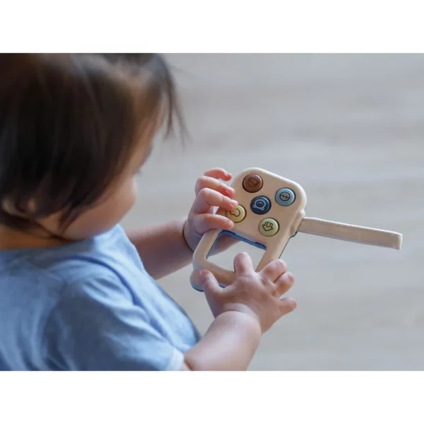 A young toddler playing with a wooden toy phone and pressing the buttons