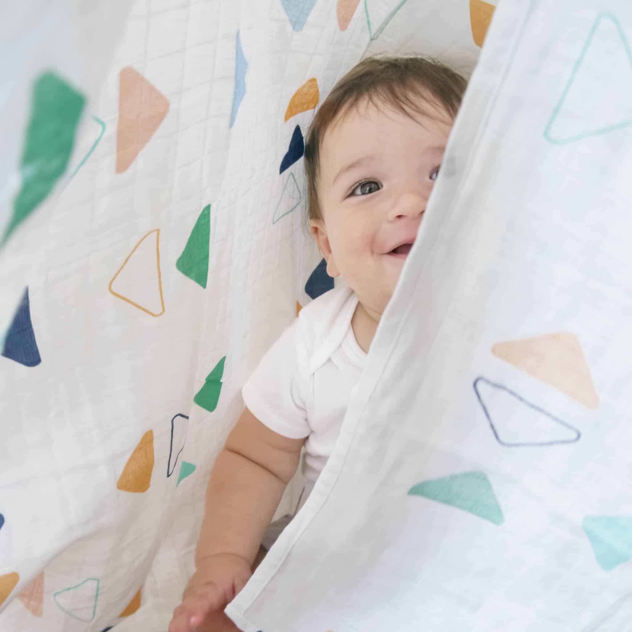 A baby smiling and wrapped in a Organic Muslin Blankets from Smartbaby Decor.