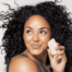 A young black woman holding a solid face soap bar up to her face and smiling.
