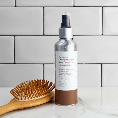 A metal bottle of hair conditioning spray with a brown and white label sitting a shower next to a washing brush.