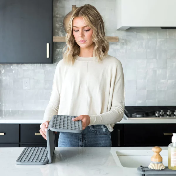 A woman standing at the sink folding her grey dish drying pad.