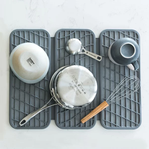 A grey dish drying pad with some cooking utensils, bowls and a pot drying on it.