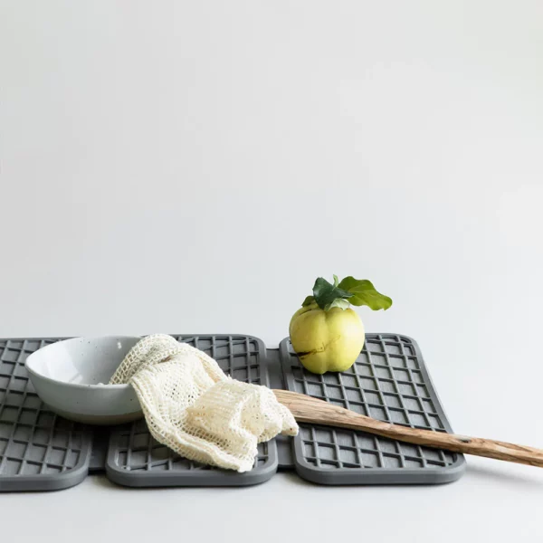 A grey dish drying pad with some cooking utensils, bowls and a pear drying on it.