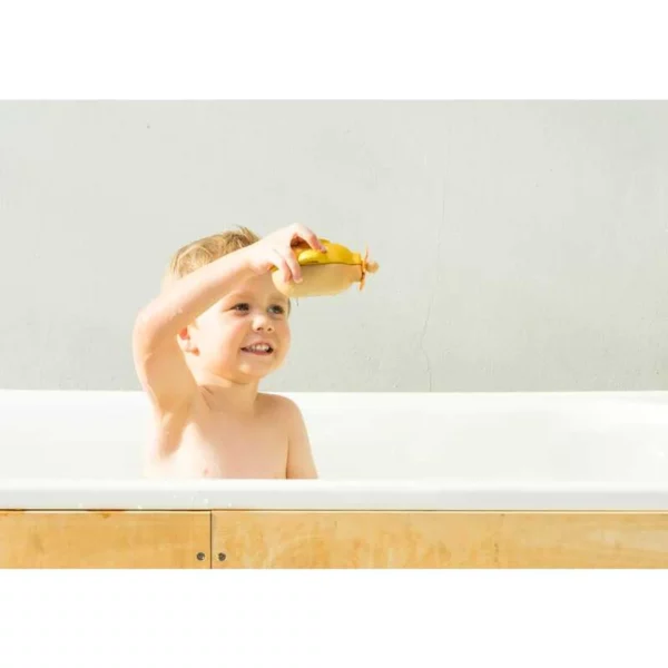 A boy in a bathtub playing with a yellow toy submarine.